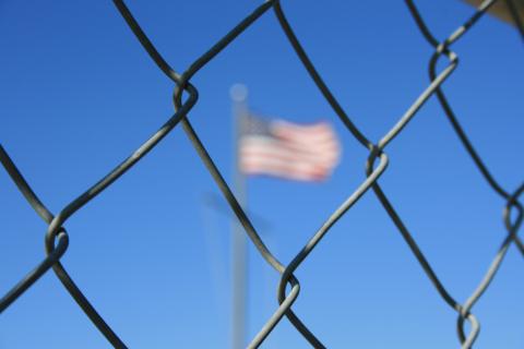 fence in foreground with a blue sky and faint USA flag in the background