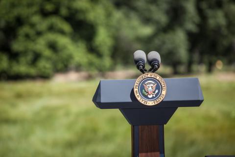 presidential podium with two microphones outdoors with grass and trees in background